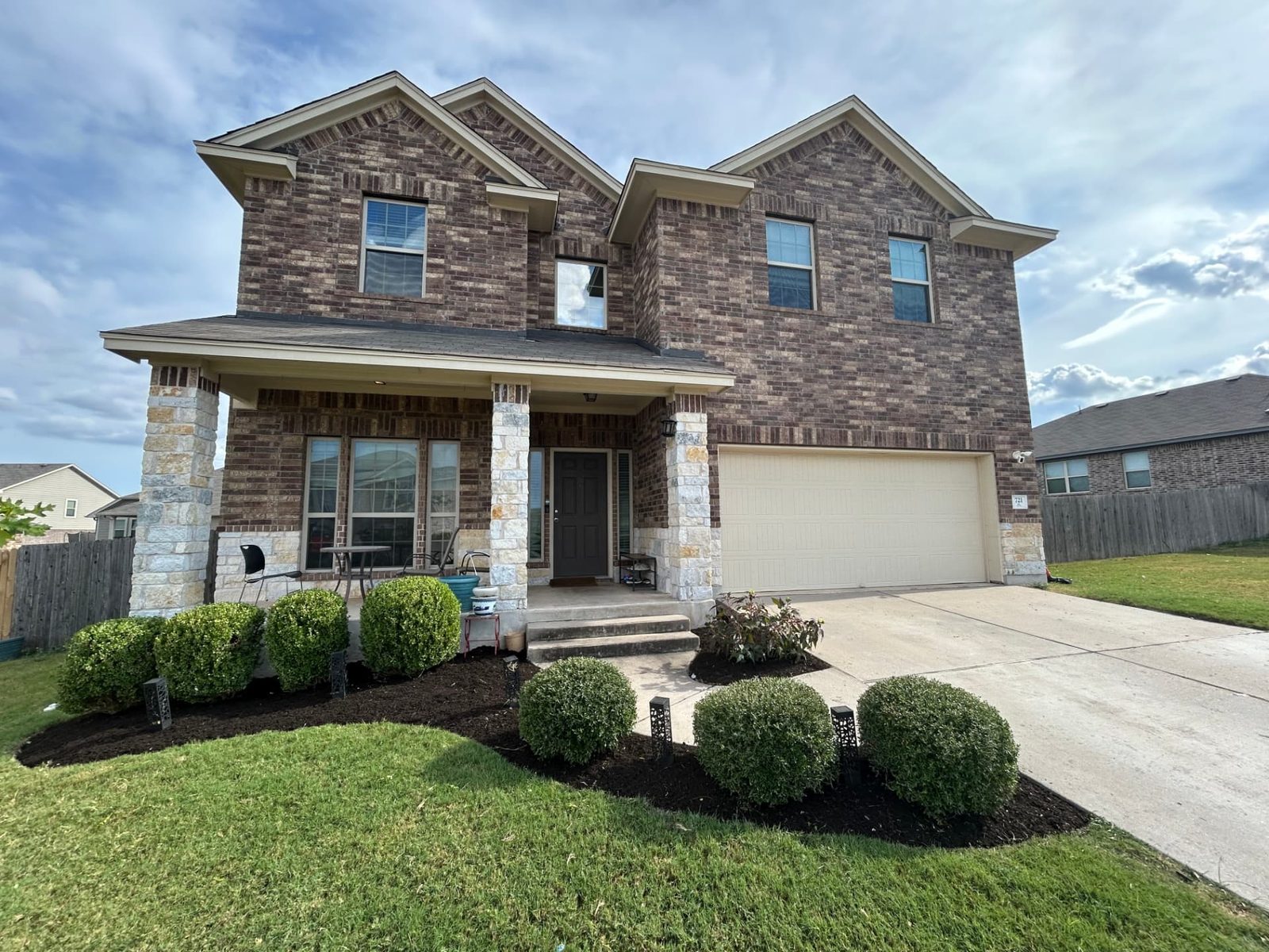 Same house with tightly trimmed rounded shrubs and fresh dark mulch