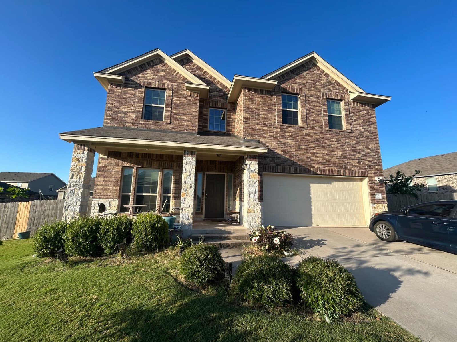 Front of brick two-story house with shaggy untrimmed shrubs and no mulch